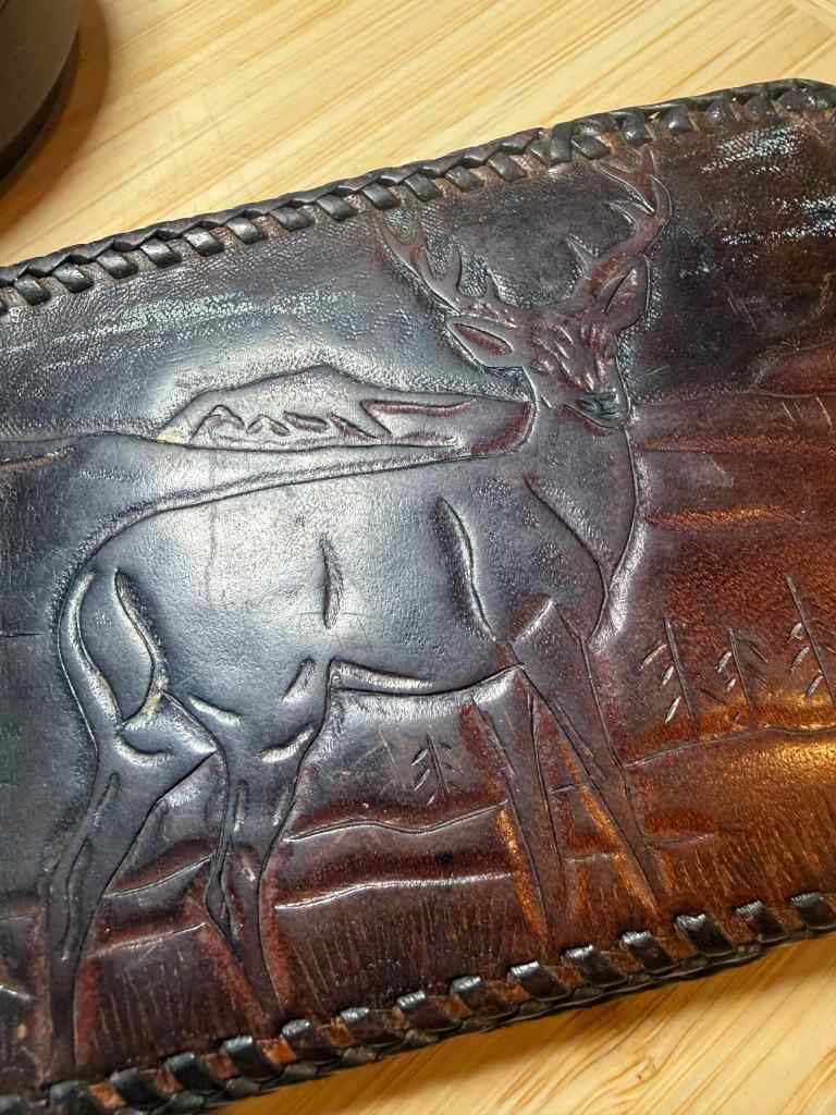 Close-up of an intricately carved leather wallet featuring a deer and mountainous landscape.